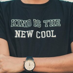 A person wearing a T-shirt with 'Kind is the New Cool' and a stylish wristwatch.